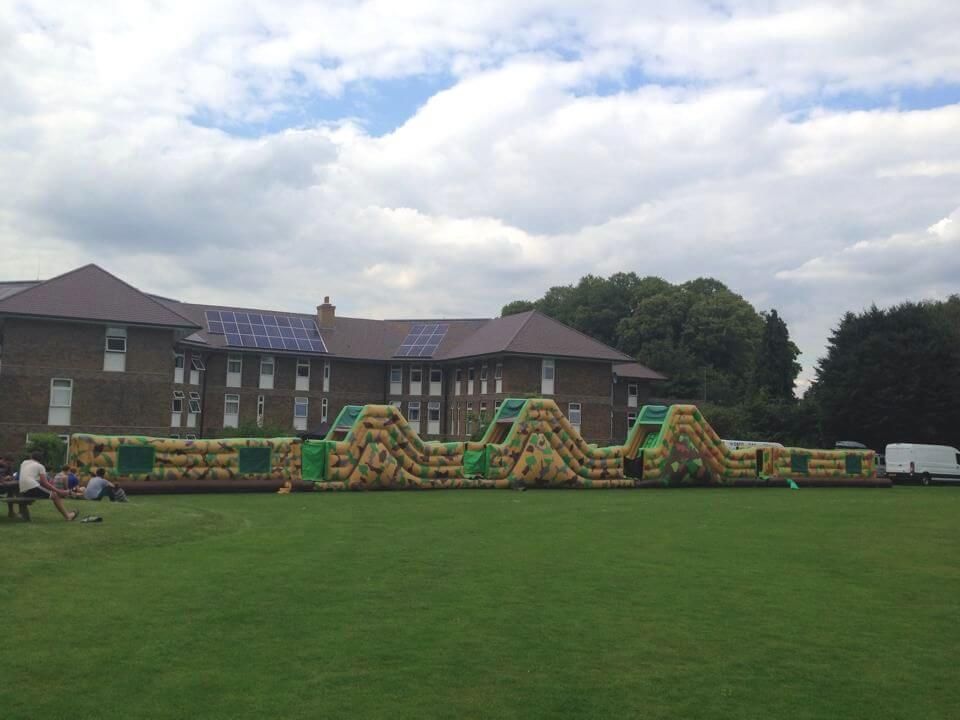 125ft army assault course in camouflage on a playing field, two slide mounds, brick building behind