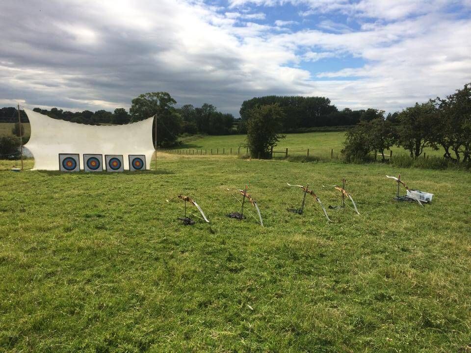 Four square archery targets with recurve bows on stands in a grassy field