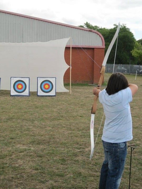 Participant drawing a recurve bow and aiming at targets on a grass field