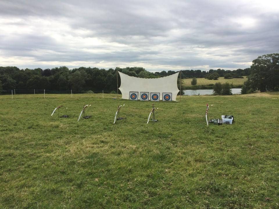 Five recurve bows on stands facing four targets across an open grass field
