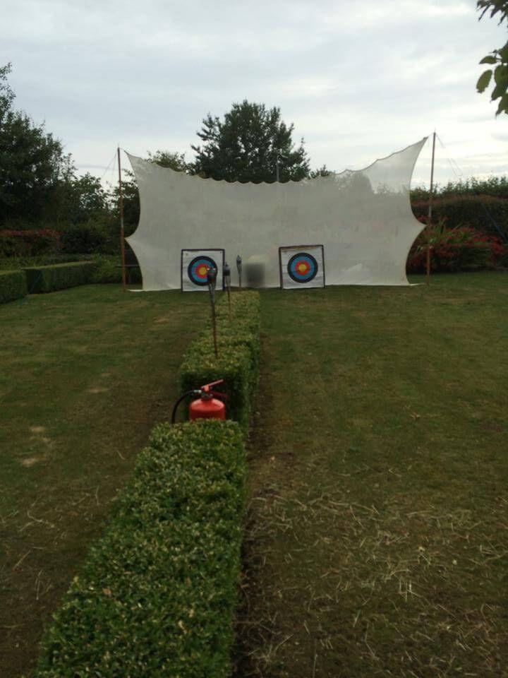 Two square archery targets with a white mesh backstop in a garden setting