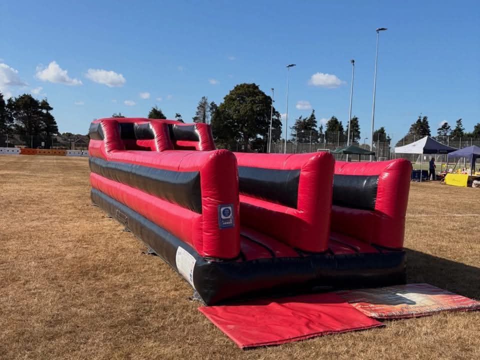 Bungee run inflated on a dry event field with canopy tents behind on a sunny day