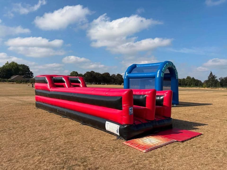 Bungee run set up on a field at a fun day beside a blue speed pitch inflatable
