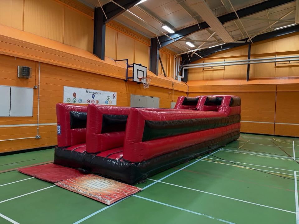 Bungee run set up indoors in a sports hall with a crash mat and rules of play sign at the front