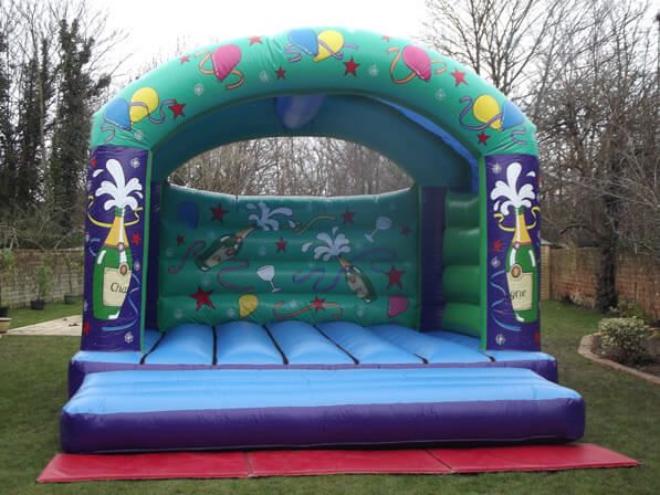 Green and purple celebration bouncy castle with balloon and champagne artwork on a lawn