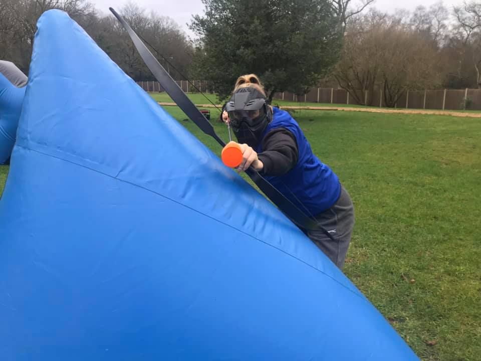 Player aiming a bow with orange foam-tipped arrow from behind a blue inflatable barrier