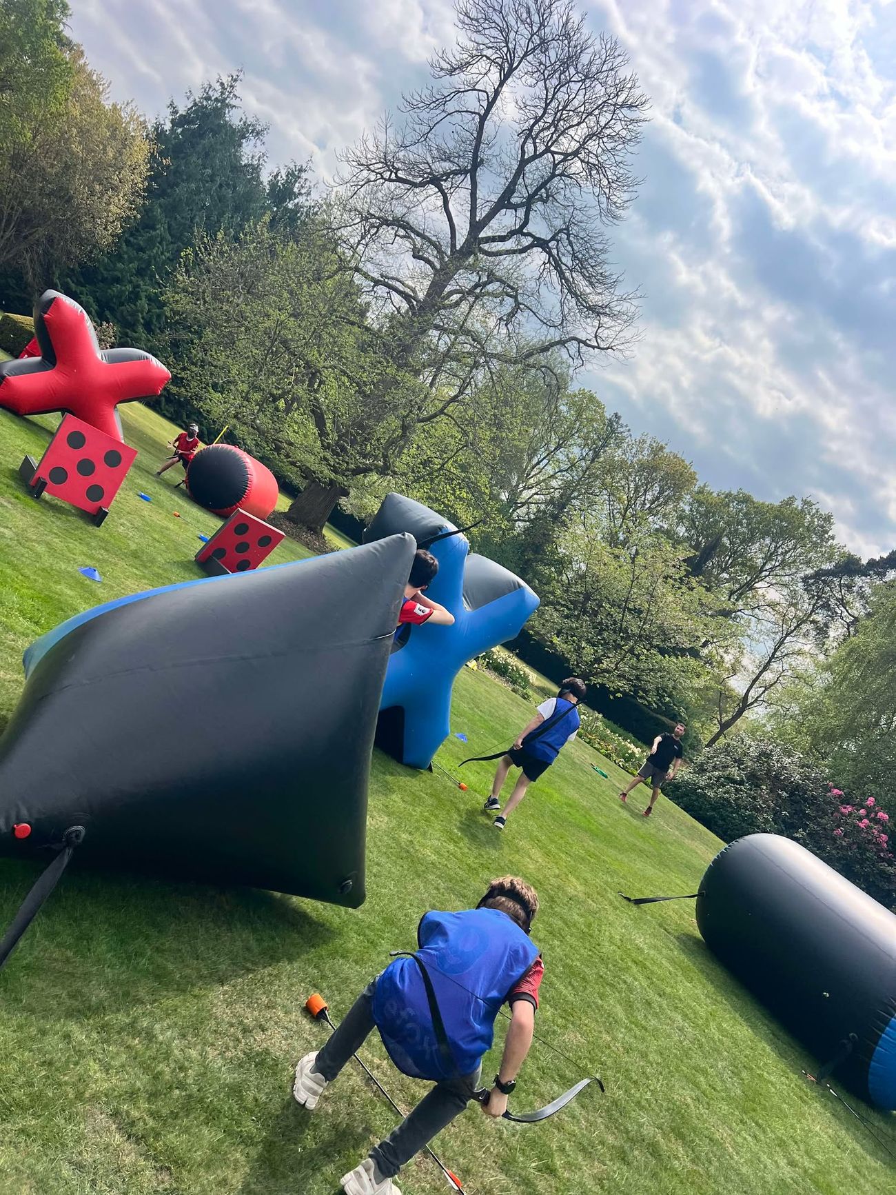 Two teams playing combat archery with foam arrows behind inflatable bunkers on a grassy field