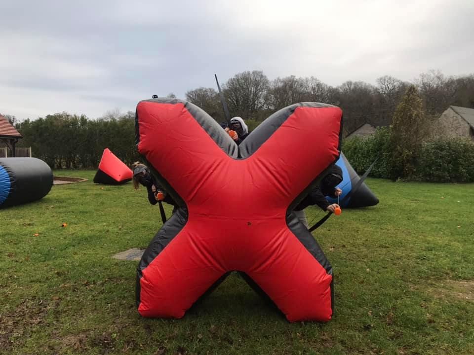 Players hiding behind a red X-shaped inflatable bunker during a tag archery game