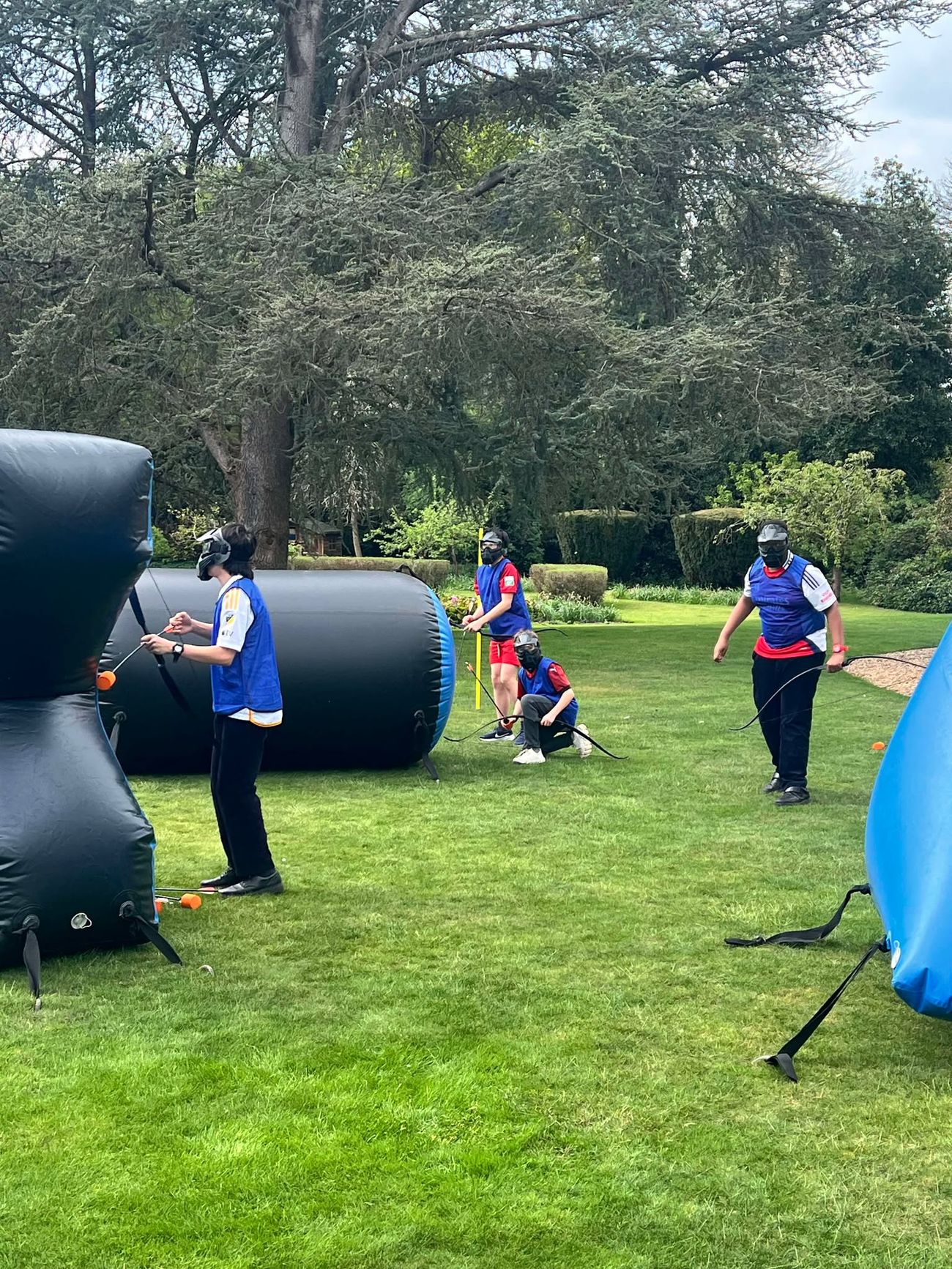 Team in blue bibs holding bows across a grassy field with inflatable bunkers