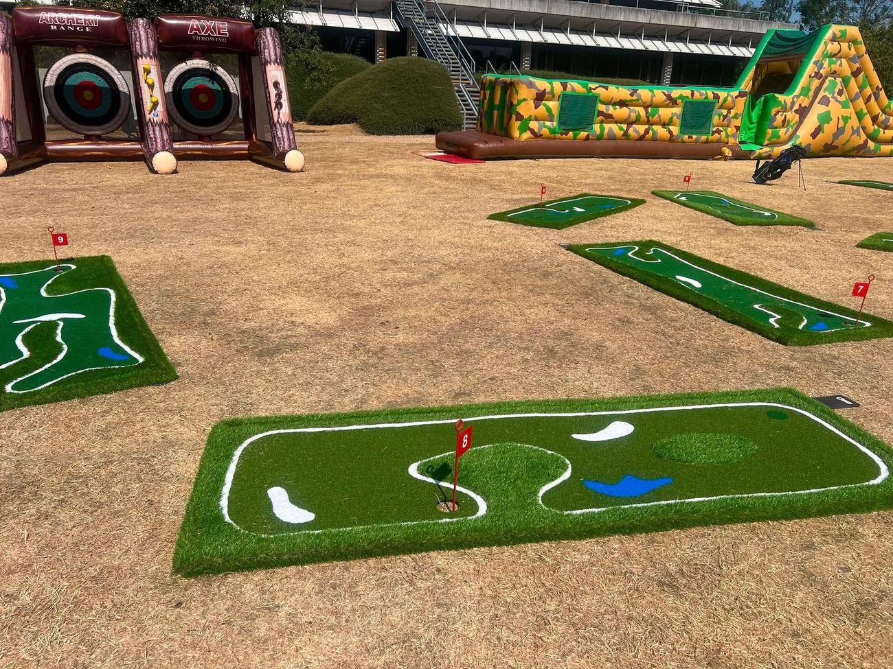 Numbered mini golf holes with painted hazards on grass outside an office building