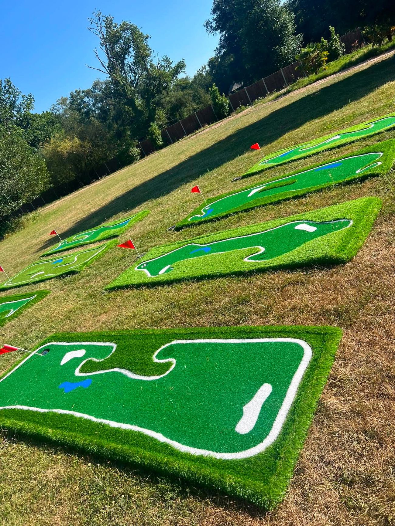 New mini golf holes with red flags laid out in staggered rows across a sunny lawn