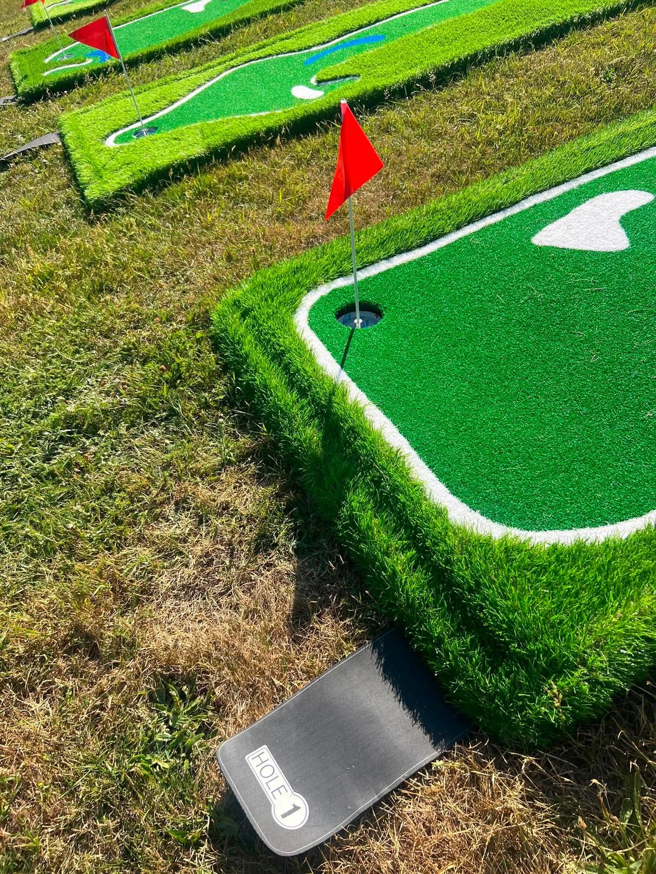 Raised mini golf holes with painted hazards and red flags receding across a grass field