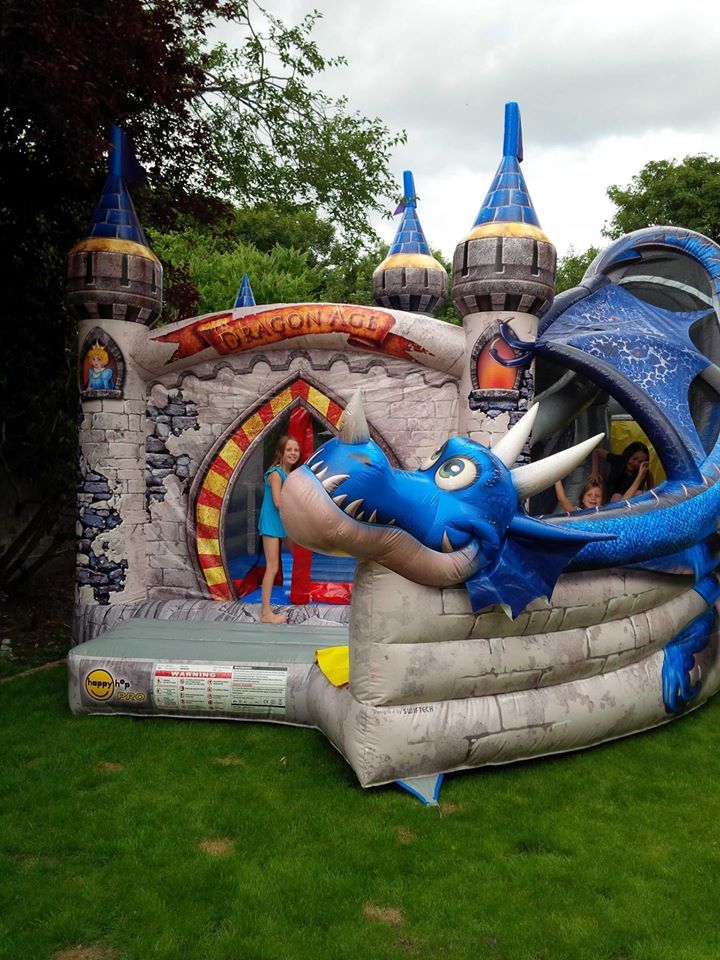 Dragon Age bouncy castle in a garden, blue dragon head and wing, child standing inside