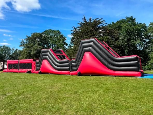 Red and black inflatable assault course on grass under a blue sky in north London