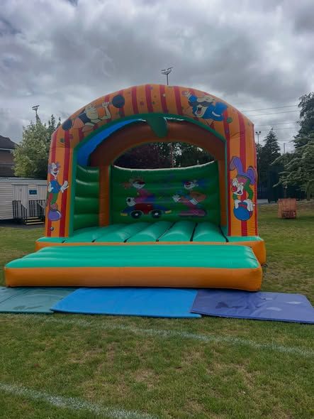 Orange and yellow bouncy castle with cartoon graphics on a school field in Surrey