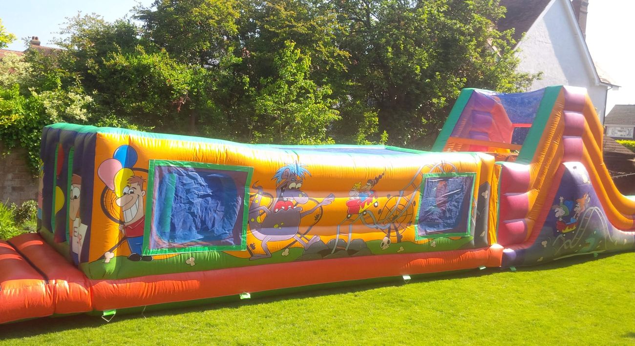 Side view of fun fair assault course on grass, orange body, green trim, cartoon clown and wolf