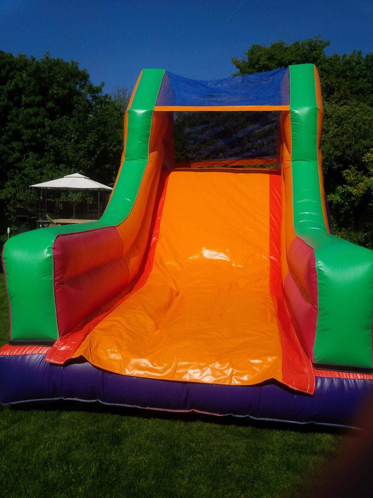 Rear exterior of inflatable slide with orange bed, green sides, purple base and blue mesh canopy