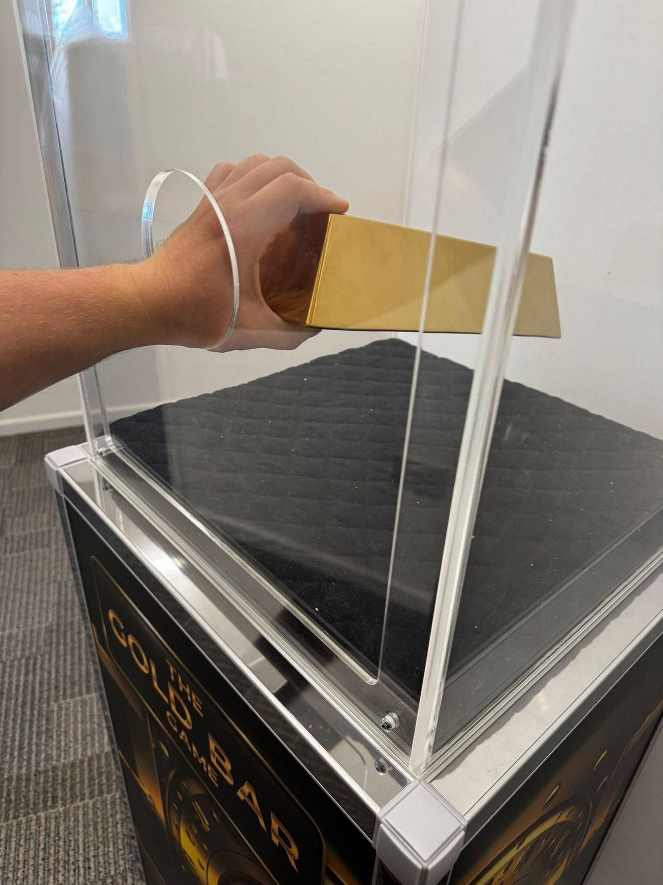Hand reaching through the hole in the case to lift the gold bar