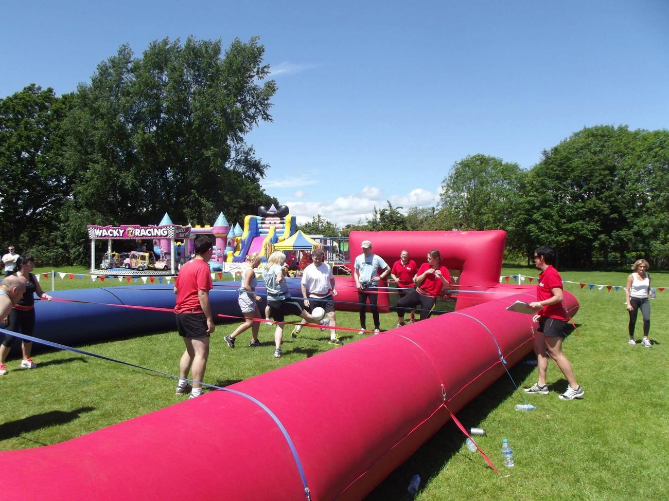 Players strapped to the ropes mid-game on the red and blue pitch at a sunny fun day