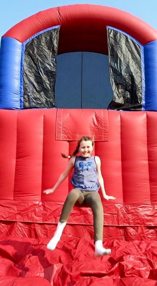 Girl in socks mid-jump from the red inflatable base jump tower against a blue sky