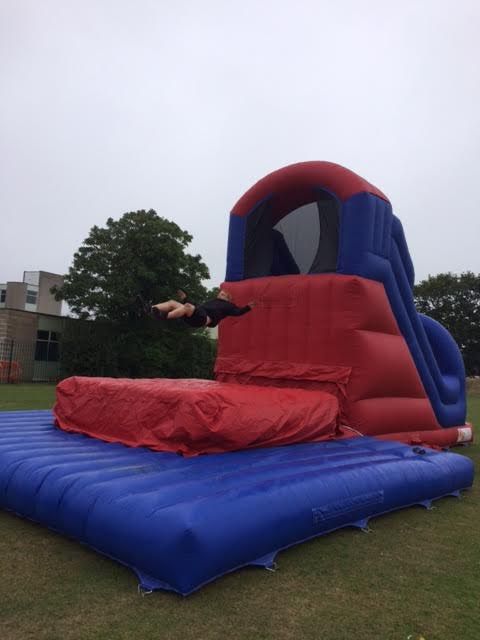 Jumper airborne above the red landing bed of the inflatable base jump, building behind