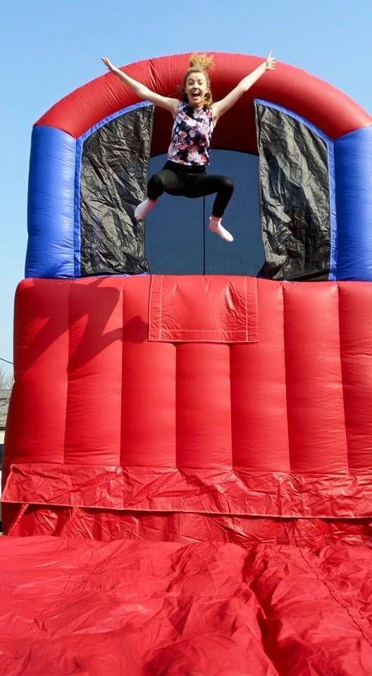 Woman leaping arms-wide from the base jump platform against a blue sky above the red landing area