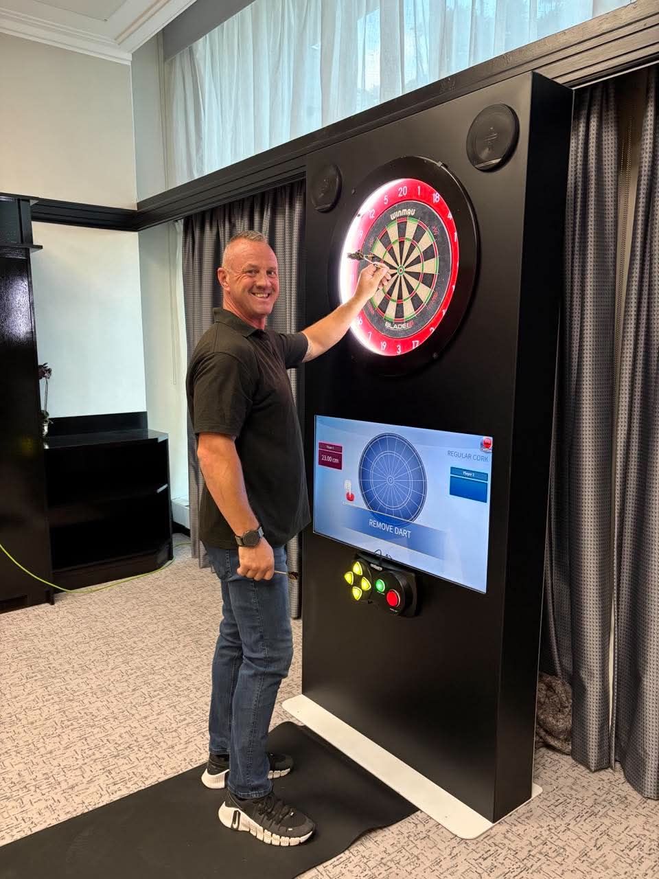 Dave from the Monster team posing with a dart beside the black interactive dartboard