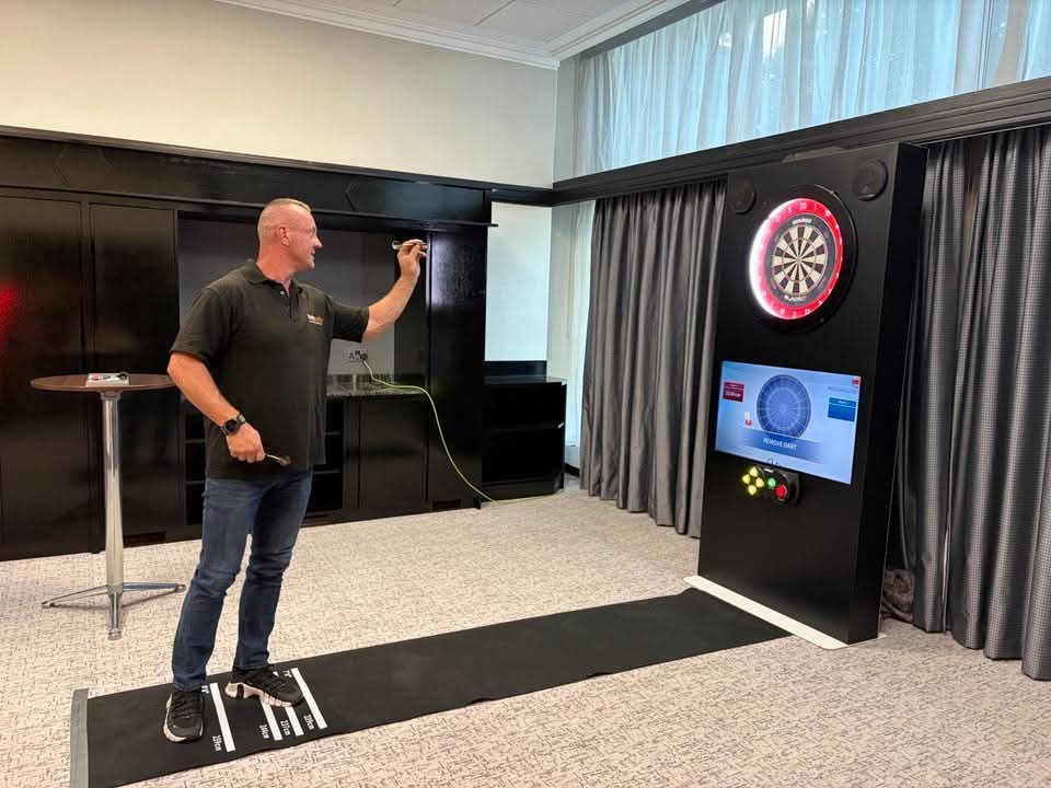 Dave throwing a dart down the marked throw mat at the black interactive dartboard