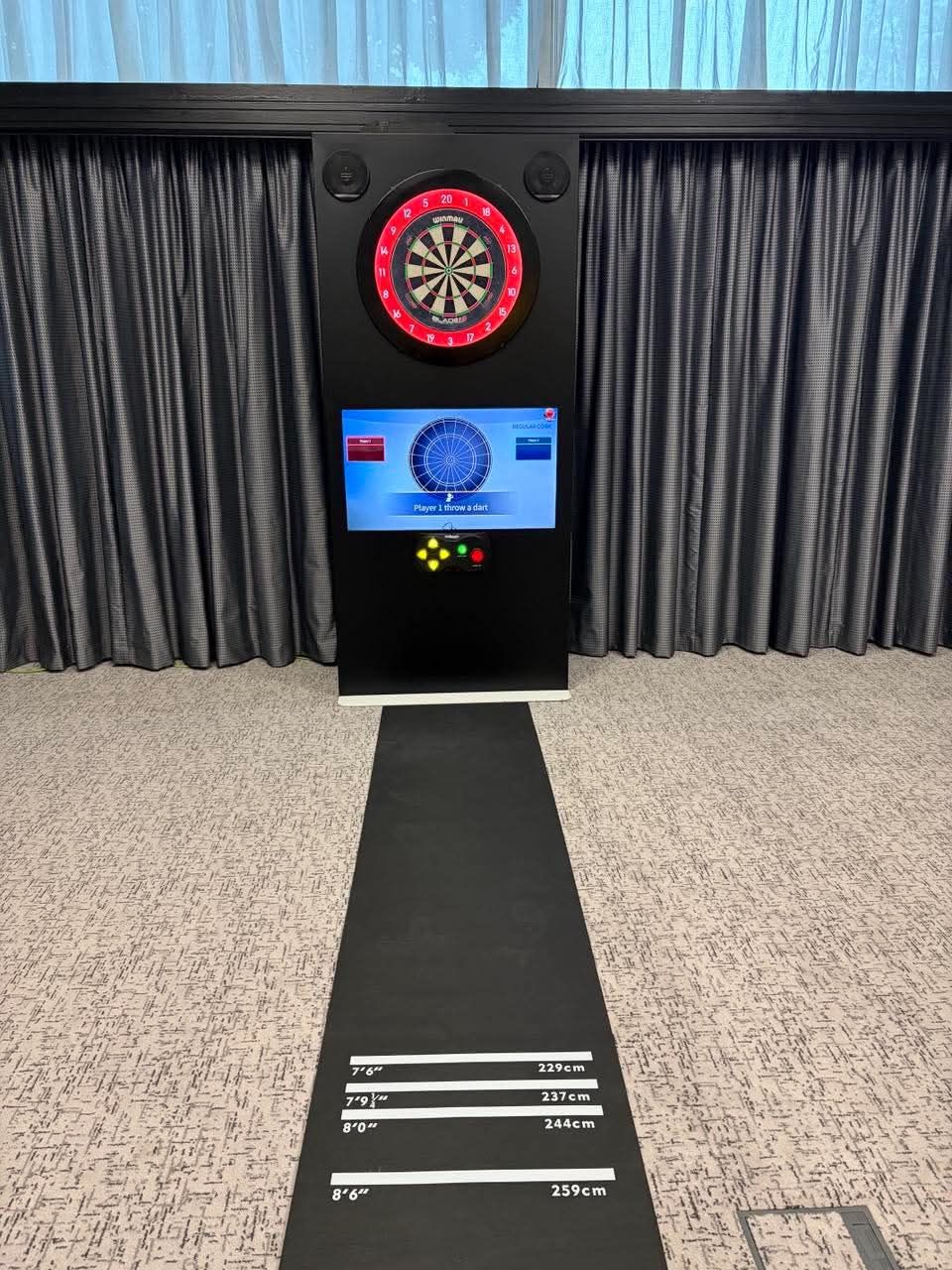 Black interactive dartboard set up in a function room with its throw mat stretched out