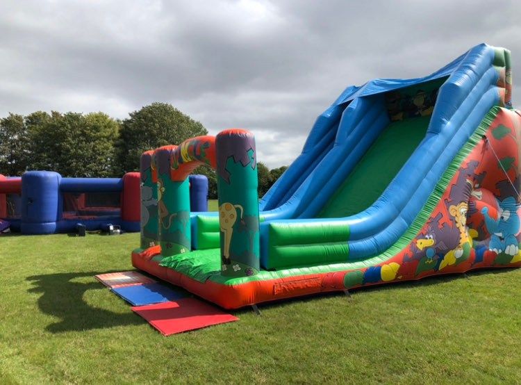 Side view of the 20ft Jungle Event Slide on grass, single blue slide bed with crash mat at the foot