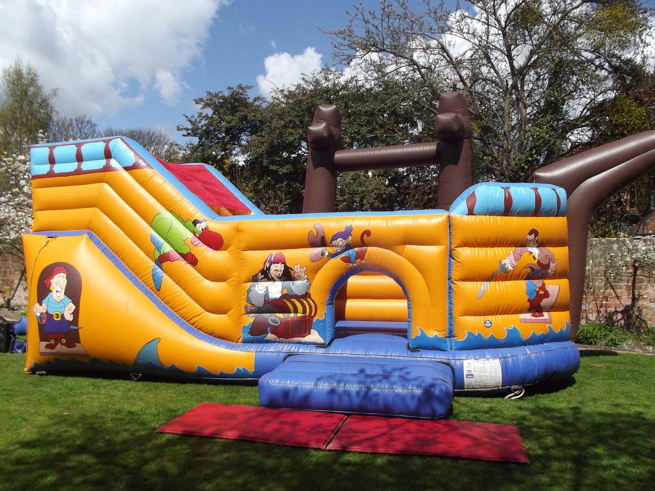 Yellow pirate ship inflatable with a slide and a bounce area, set up on grass