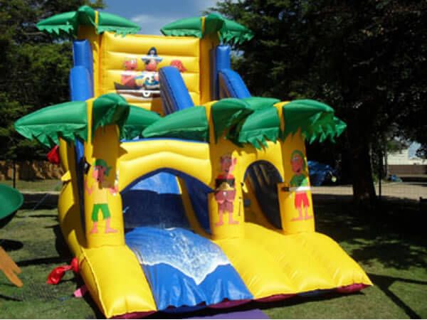 Yellow pirate-themed inflatable mega slide with palm trees and a blue slide lane, set up on grass