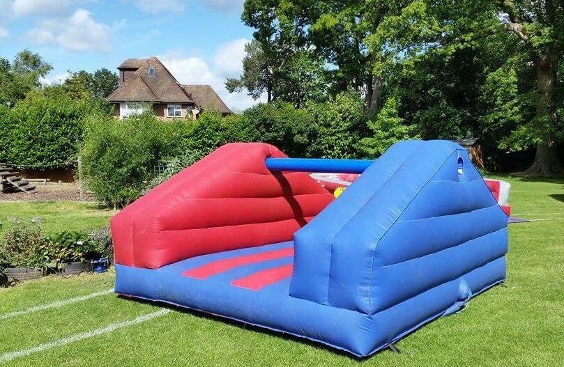 Red and blue pole jousting inflatable on a lawn, with the central pole and padded sections either side