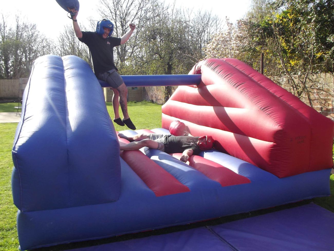 Player in a blue head guard celebrating after knocking his opponent onto the padded inflatable bed