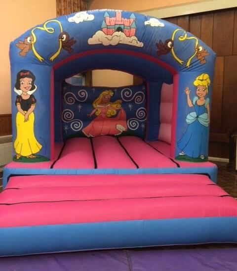 Pink and blue princess bouncy castle with fairytale artwork on the pillars, set up in a hall