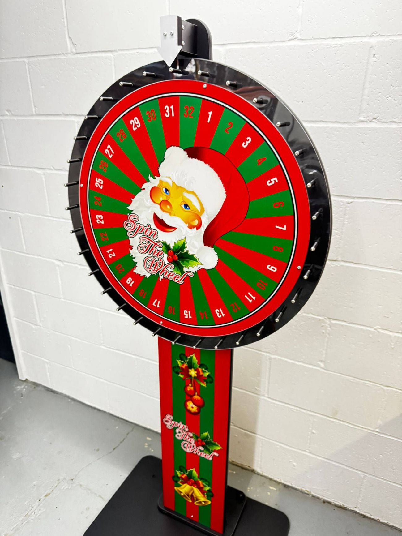 Christmas prize wheel with 32 numbered red and green segments, Santa centre, on a stand