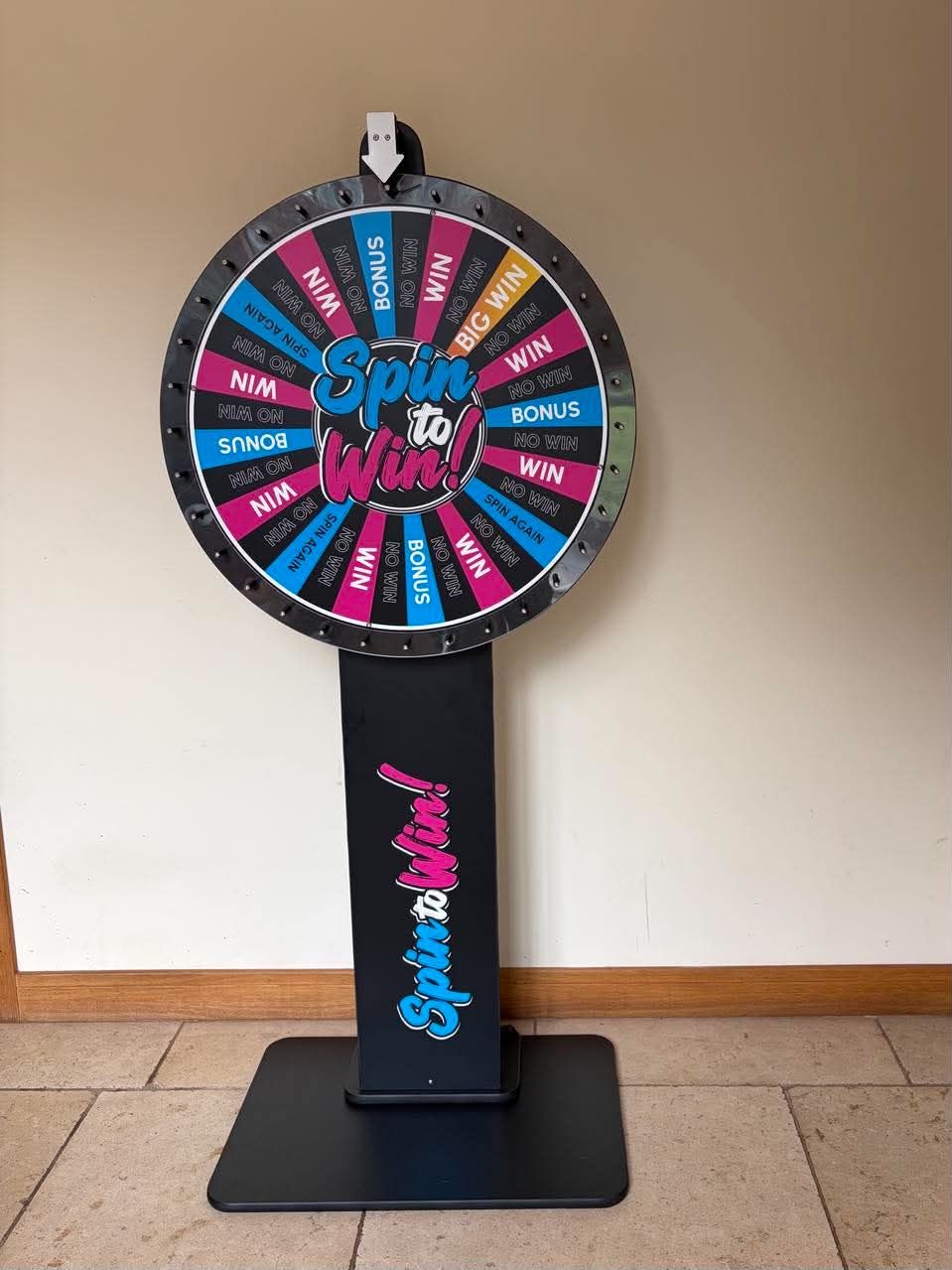 Spin to Win prize wheel with pink and blue WIN, BONUS and NO WIN segments on a black stand