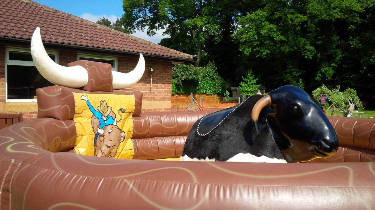 Black mechanical bull with saddle in brown inflatable arena with cartoon cowboy panel