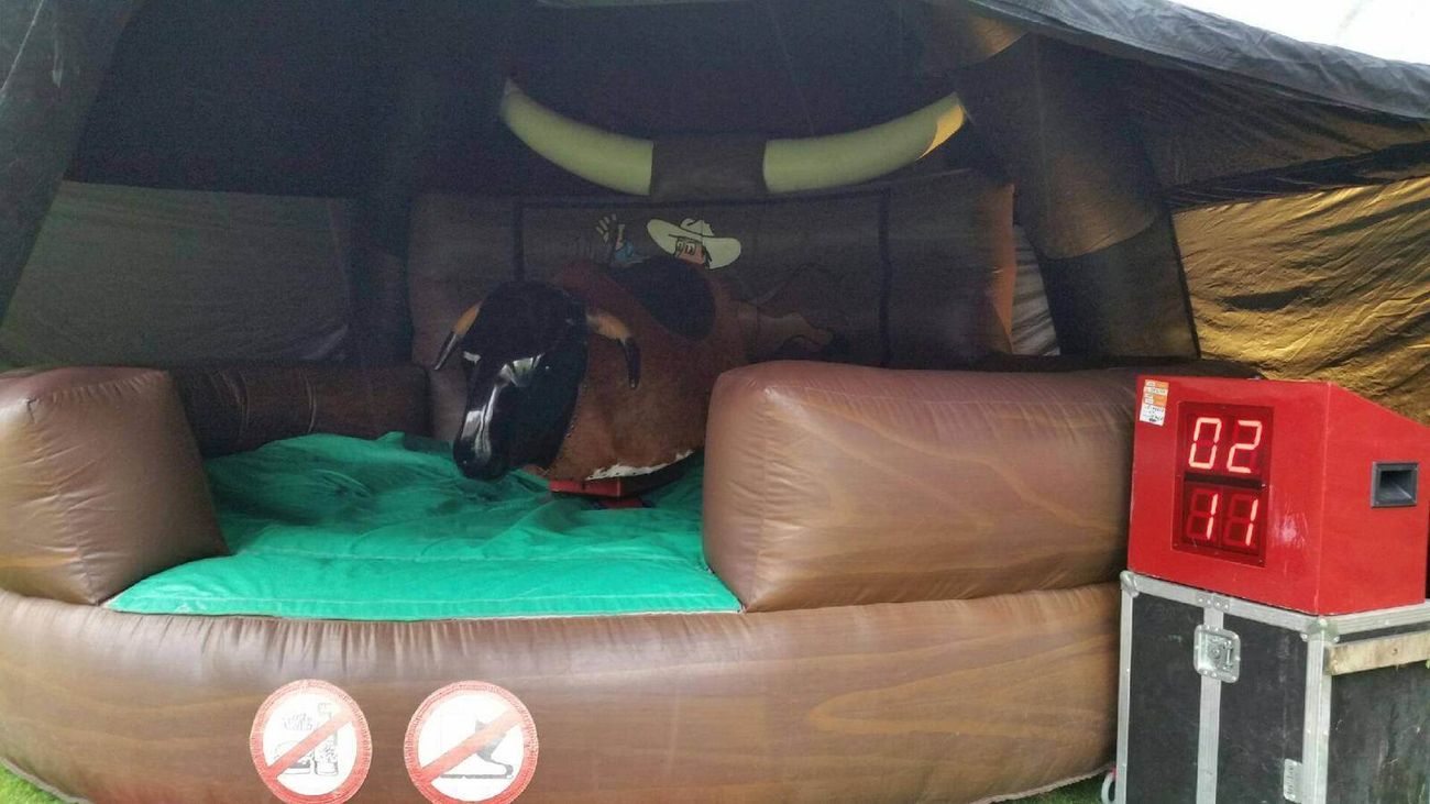 Mechanical bull on green mat inside brown inflatable arena with red LED timer and cartoon backdrop
