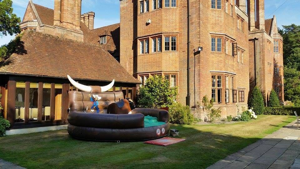 Mechanical bull ride with brown bull and white horns on a lawn before a brick manor house