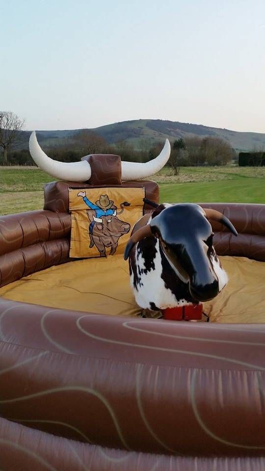 Mechanical bull with black head and brown horns in inflatable arena with cartoon cowboy backdrop