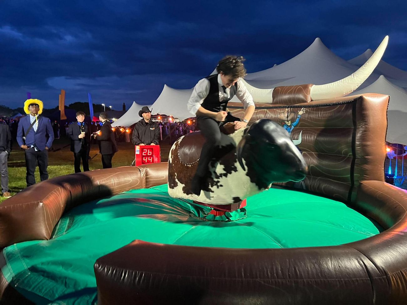 Mechanical rodeo bull set up at an evening outdoor event with inflatable surround and timer