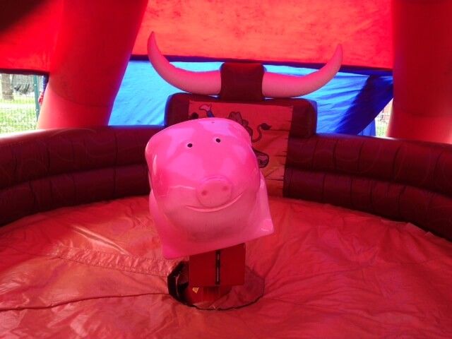 Front-on view of the smiling pink rodeo pig inside the red horned inflatable surround