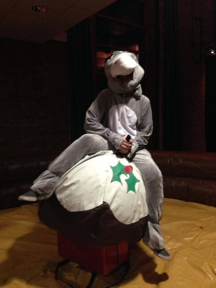 Rider in a grey onesie holding on to the Christmas pudding rodeo at a dimly lit party venue