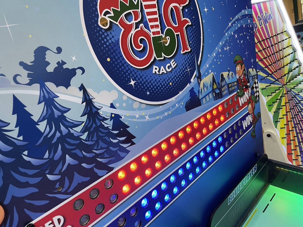 Elf Race scoreboard with red and blue LED tracks, a snowy village and a cartoon running elf
