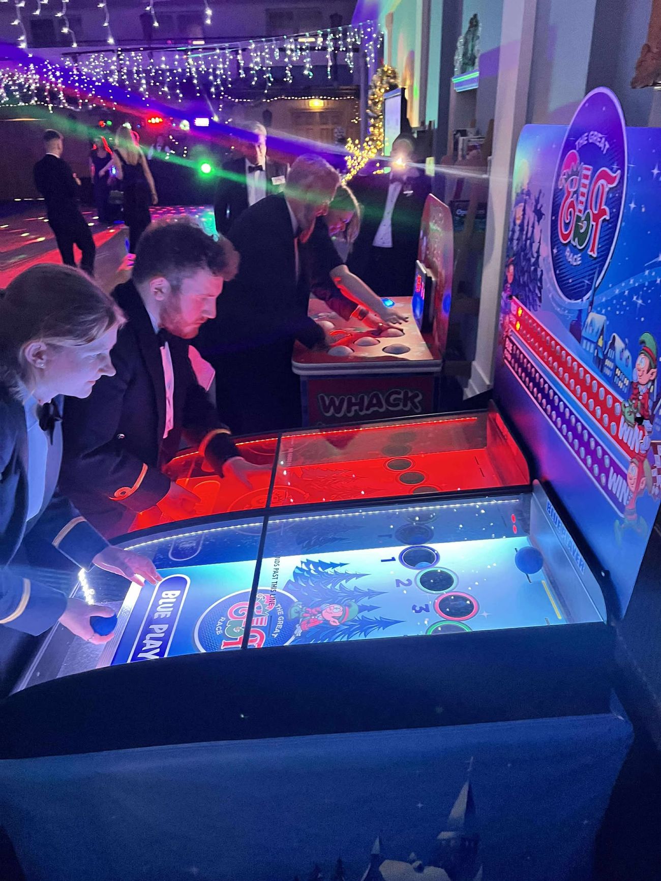 Elf Racing Derby beside a Whack an Elf game with black-tie guests at an office Christmas party
