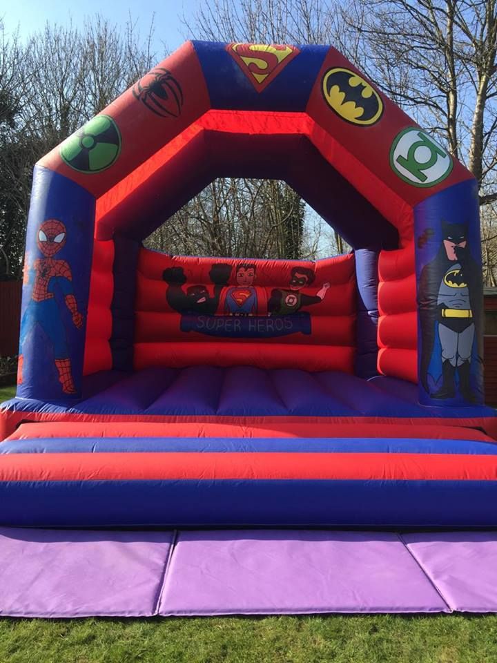 Red and blue superhero bouncy castle with Spider-Man and Batman artwork, set up on grass
