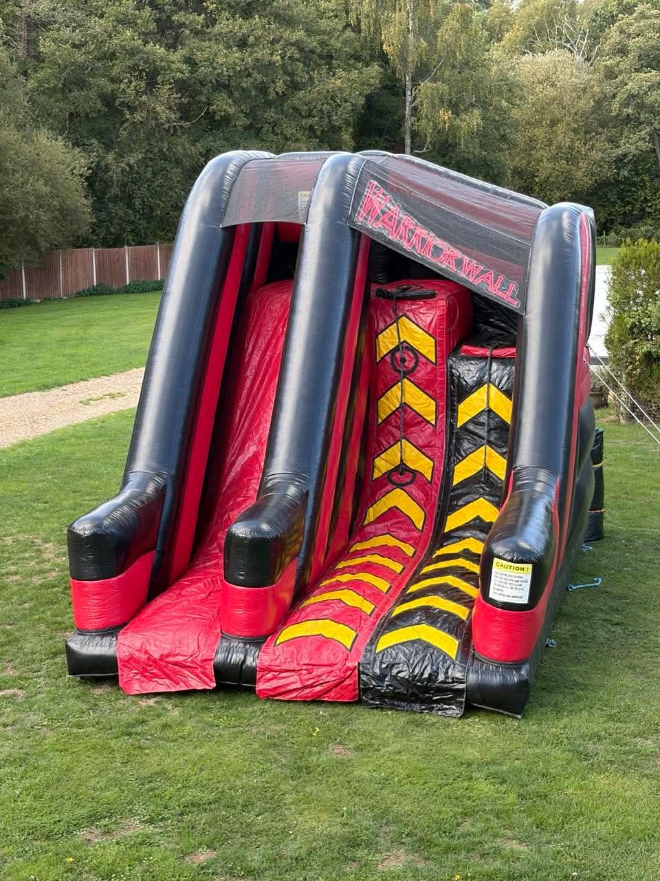 Red and black Warrior Wall inflatable twin lane climbing wall set up on grass