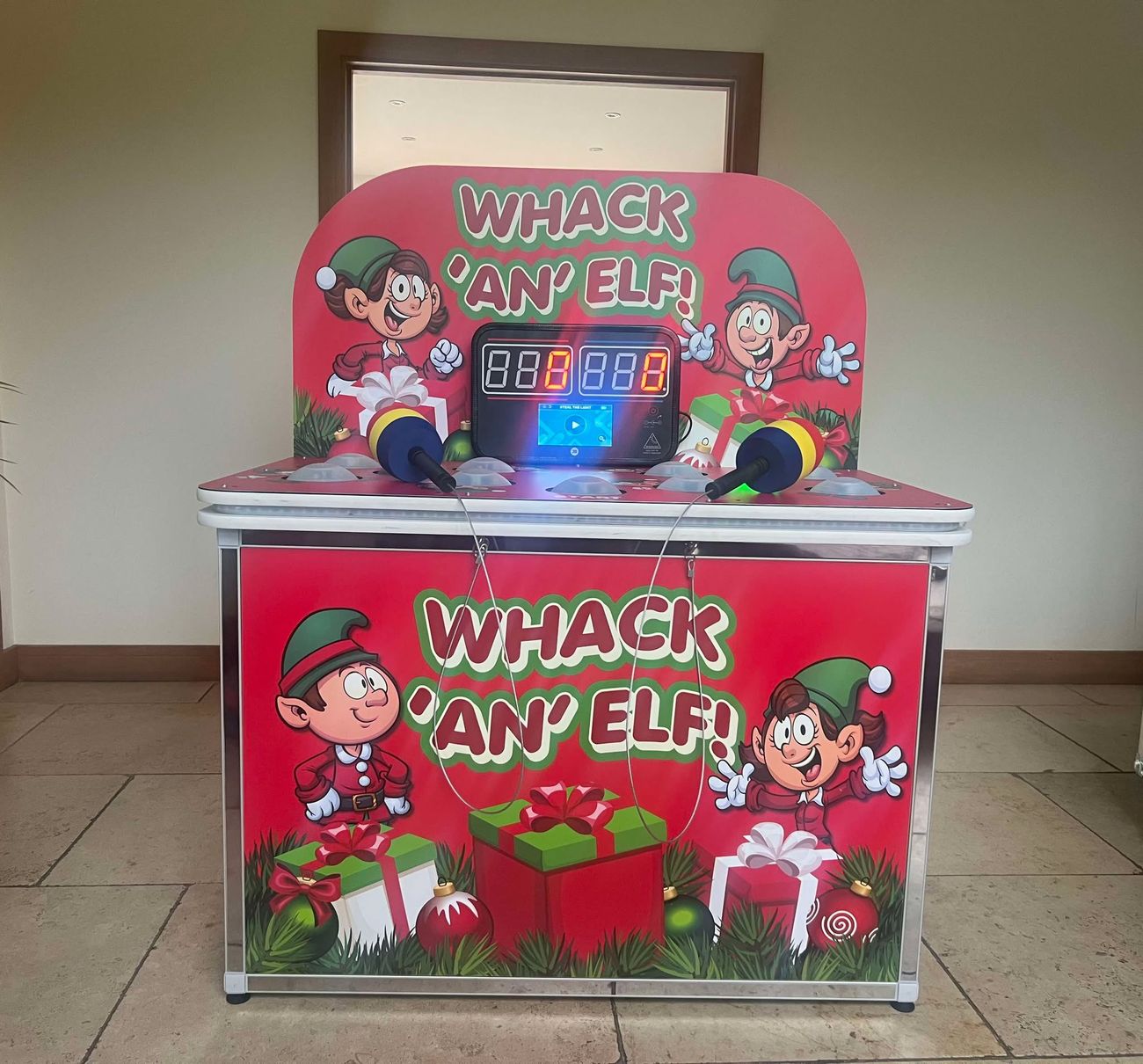 Red Whack an Elf cabinet with elf artwork, digital scoreboard and two padded mallets resting on the dome playfield