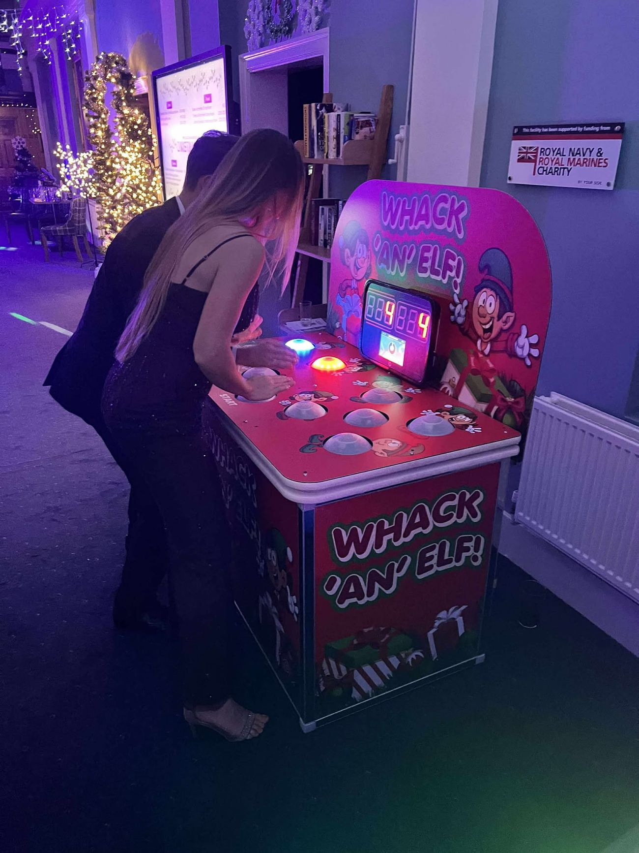 Two guests in evening wear leaning over the lit-up Whack an Elf game at a Christmas party